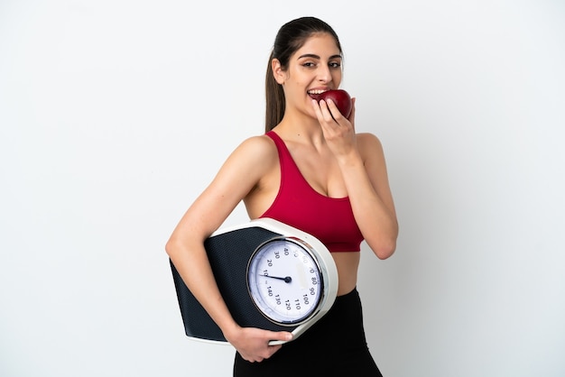 Young caucasian woman isolated on white background with weighing machine and with an apple