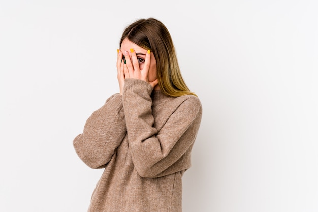 Young caucasian woman isolated on white blink through fingers frightened and nervous.