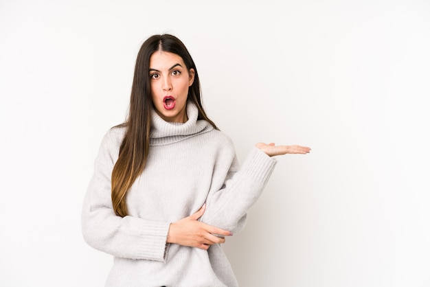 Young caucasian woman isolated on a white surface impressed holding copy space on palm.