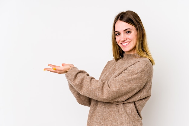 Young caucasian woman isolated on white wall holding a copy space on a palm.
