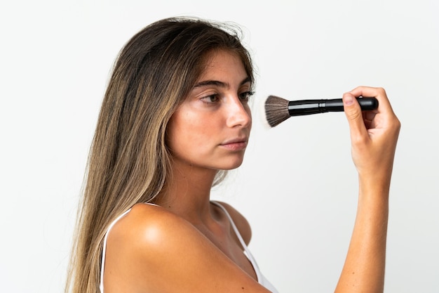 Young caucasian woman isolated on white wall holding makeup brush