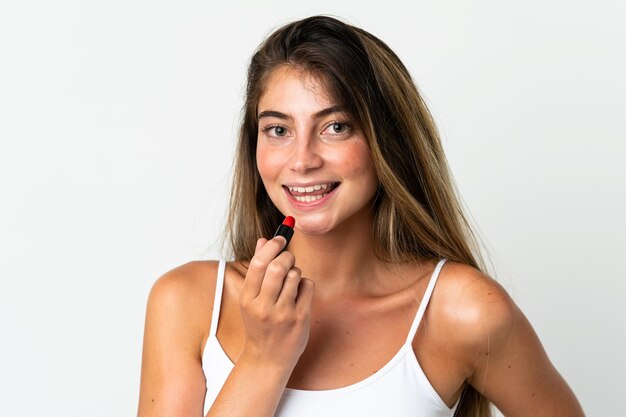 Young caucasian woman isolated on white wall holding red lipstick