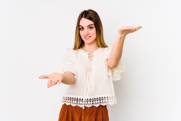 Young caucasian woman isolated on white wall makes scale with arms, feels happy and confident.