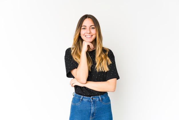 Young caucasian woman isolated on white wall smiling happy and confident, touching chin with hand.