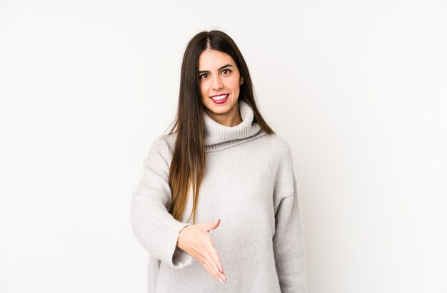 Young caucasian woman isolated on a white wall stretching hand at in greeting gesture.