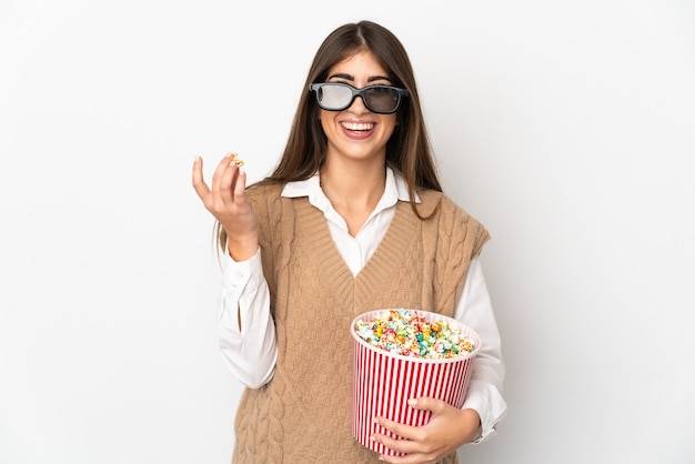 Young caucasian woman isolated on white wall with 3d glasses and holding a big bucket of popcorns