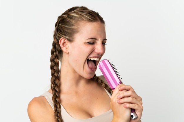 Young caucasian woman isolated on white with hair comb and singing