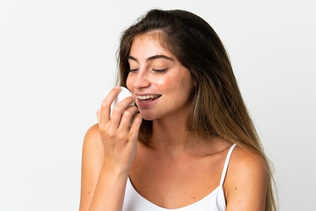 Young caucasian woman isolated on white with moisturizer and smelling it