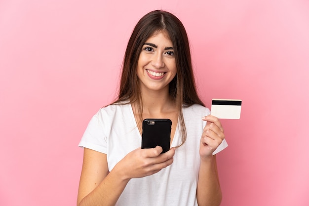 Young caucasian woman isolated with the mobile with a credit card