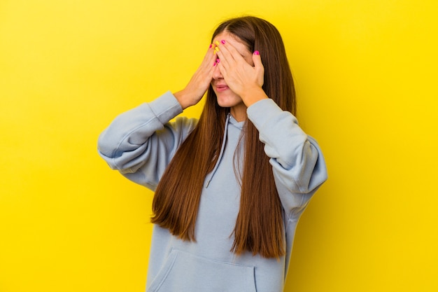 Young caucasian woman isolated on yellow background afraid covering eyes with hands.