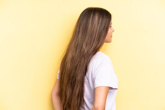 young caucasian woman isolated on yellow background in back position and looking back