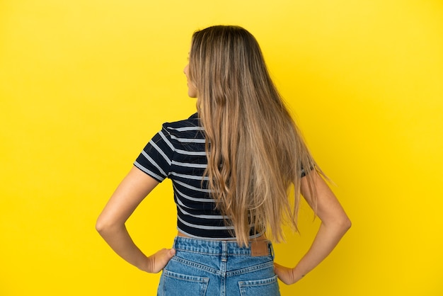 Young caucasian woman isolated on yellow background in back position and looking side