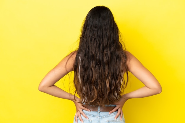 Young caucasian woman isolated on yellow background in back position