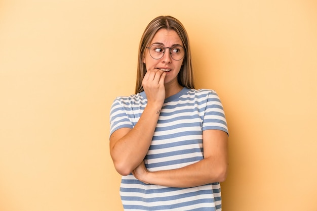 Young caucasian woman isolated on yellow background biting fingernails, nervous and very anxious.