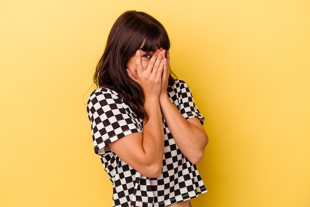 Photo young caucasian woman isolated on yellow background blink through fingers frightened and nervous.