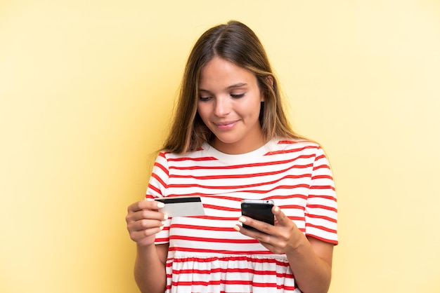 クレジットカードで携帯電話で購入黄色の背景に分離された若い白人女性