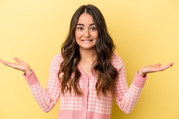 Young caucasian woman isolated on yellow background confused and doubtful shrugging shoulders to hold a copy space.