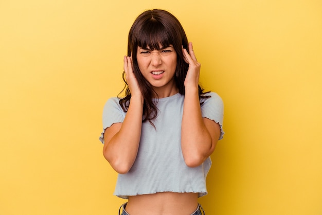 Young caucasian woman isolated on yellow background covering ears with fingers, stressed and desperate by a loudly ambient.