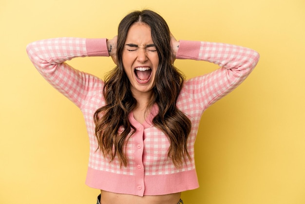 Young caucasian woman isolated on yellow background covering ears with hands trying not to hear too loud sound