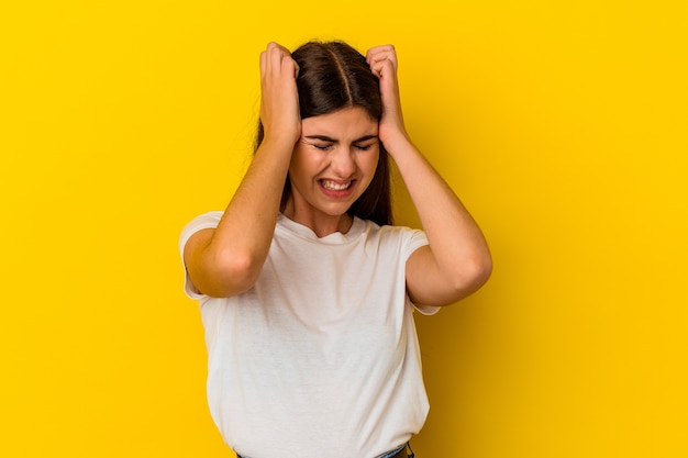 Young caucasian woman isolated on yellow background covering ears with hands.