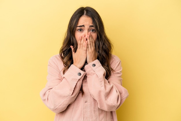 Young caucasian woman isolated on yellow background covering mouth with hands looking worried