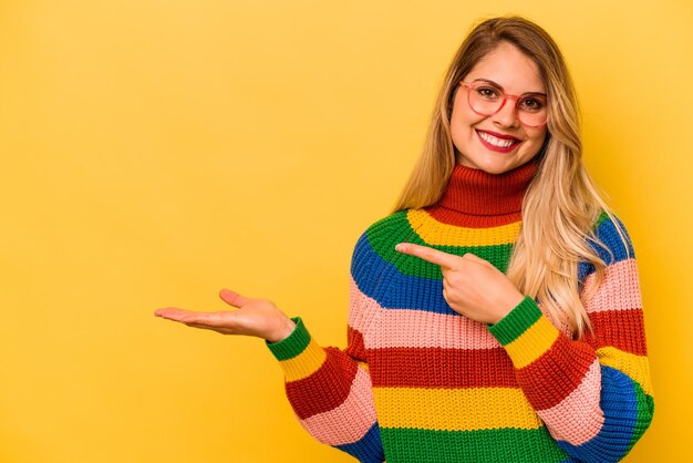 Young caucasian woman isolated on yellow background excited holding a copy space on palm