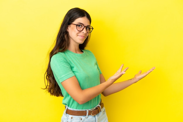 Young caucasian woman isolated on yellow background extending hands to the side for inviting to come