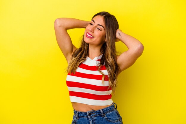 Young caucasian woman isolated on yellow background feeling confident, with hands behind the head.