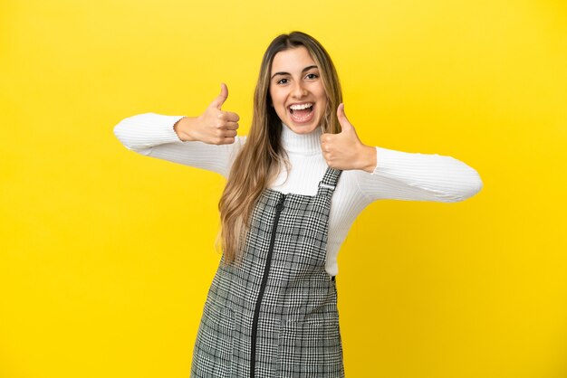 Young caucasian woman isolated on yellow background giving a thumbs up gesture