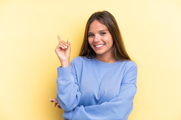 Young caucasian woman isolated on yellow background happy and pointing up