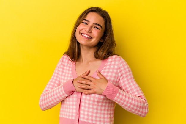 Young caucasian woman isolated on yellow background has friendly expression, pressing palm to chest. Love concept.