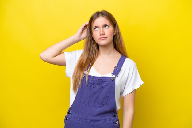 Young caucasian woman isolated on yellow background having doubts while scratching head