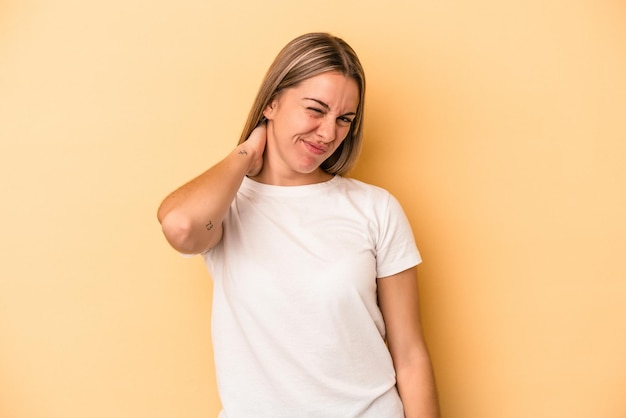 Young caucasian woman isolated on yellow background having a neck pain due to stress, massaging and touching it with hand.