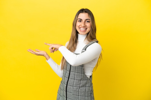 Young caucasian woman isolated on yellow background holding copyspace imaginary on the palm to insert an ad