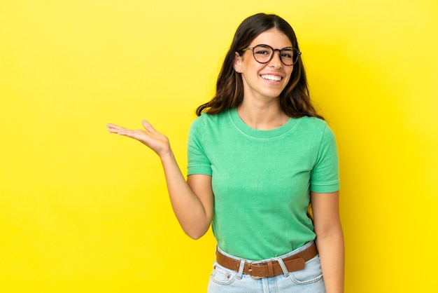 Young caucasian woman isolated on yellow background holding copyspace imaginary on the palm to insert an ad