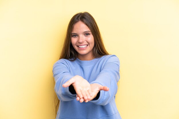 Young caucasian woman isolated on yellow background holding copyspace imaginary on the palm to insert an ad