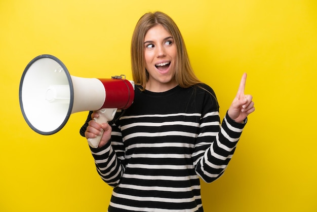 Young caucasian woman isolated on yellow background holding a megaphone and intending to realizes the solution