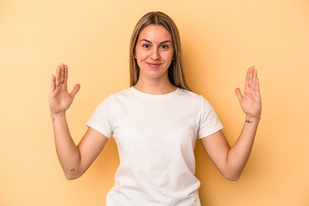 Young caucasian woman isolated on yellow background holding something little with forefingers, smiling and confident.