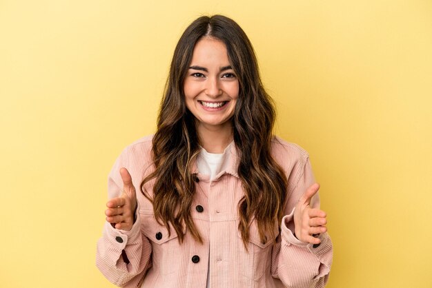 Young caucasian woman isolated on yellow background holding something with both hands product presentation