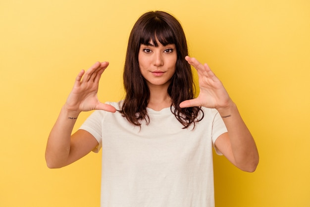 Foto giovane donna caucasica isolata su sfondo giallo che tiene qualcosa con le palme, offrendo alla telecamera.