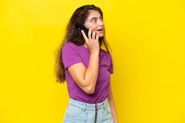 Young caucasian woman isolated on yellow background keeping a conversation with the mobile phone