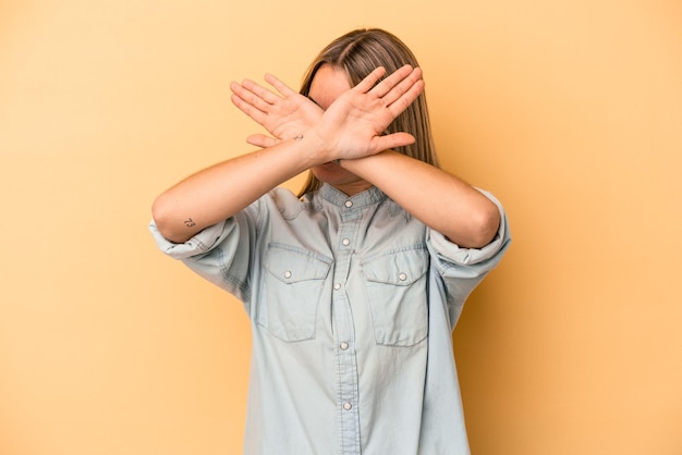 Young caucasian woman isolated on yellow background keeping two\
arms crossed, denial concept.