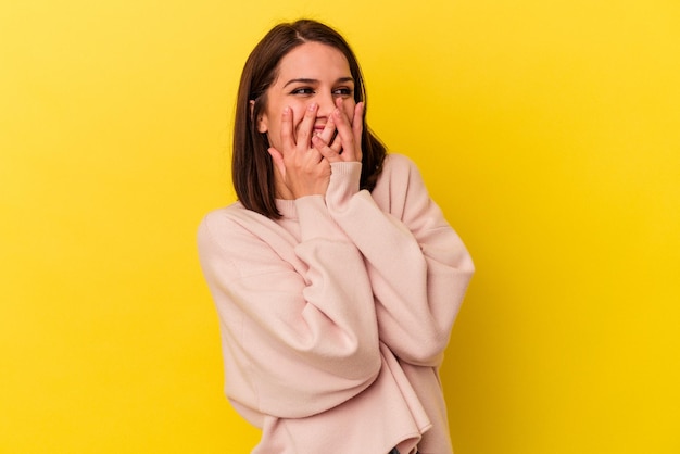 Young caucasian woman isolated on yellow background laughing about something covering mouth with hands