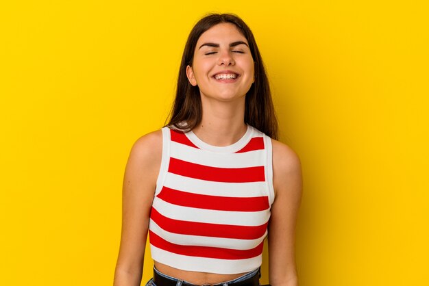 Young caucasian woman isolated on yellow background laughs and closes eyes, feels relaxed and happy.