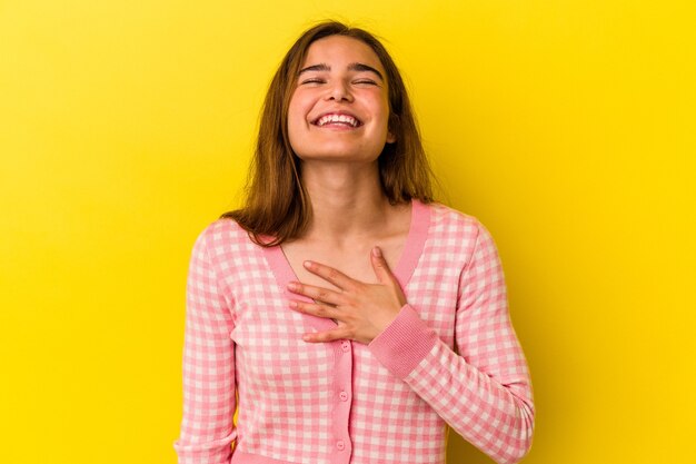 Young caucasian woman isolated on yellow background laughs out loudly keeping hand on chest.