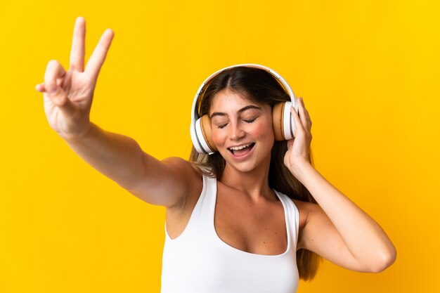 Young caucasian woman isolated on yellow background listening music and singing