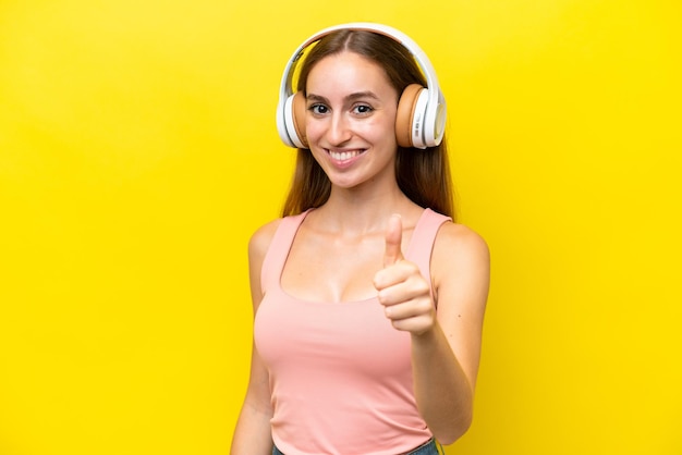 Young caucasian woman isolated on yellow background listening music and with thumb up