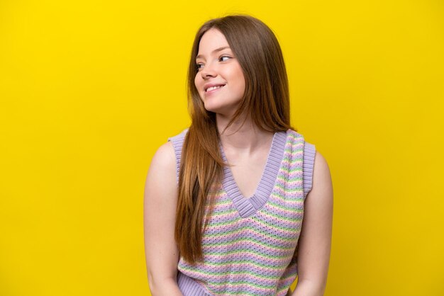 Young caucasian woman isolated on yellow background looking to the side and smiling