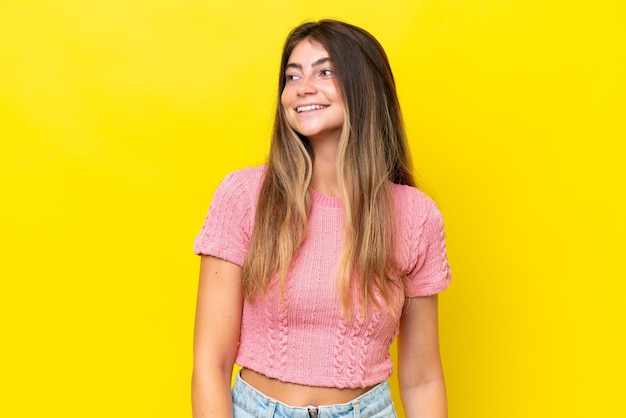 Young caucasian woman isolated on yellow background looking to the side and smiling