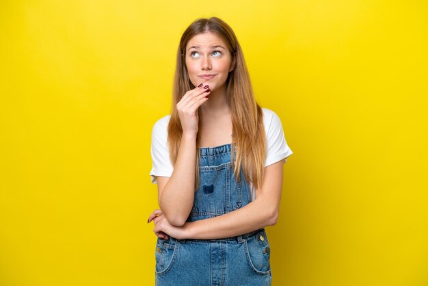 Young caucasian woman isolated on yellow background looking up while smiling